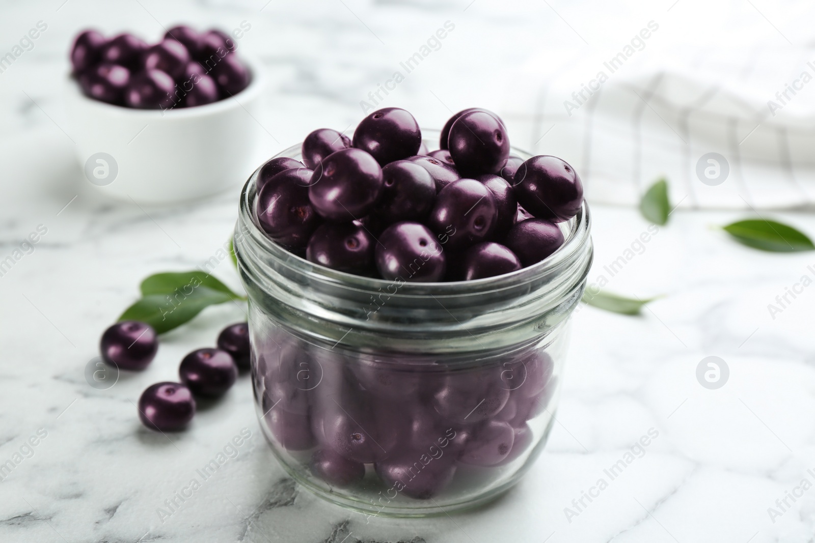 Photo of Fresh acai berries in glass jar on white marble table, closeup