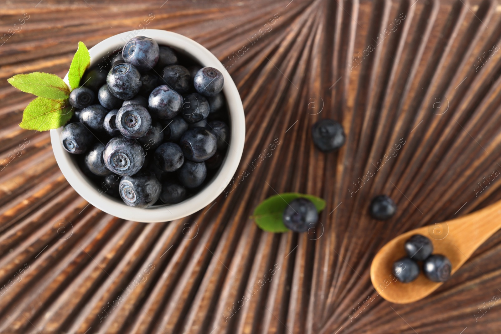 Photo of Tasty fresh bilberries and green leaves on wooden table, flat lay. Space for text