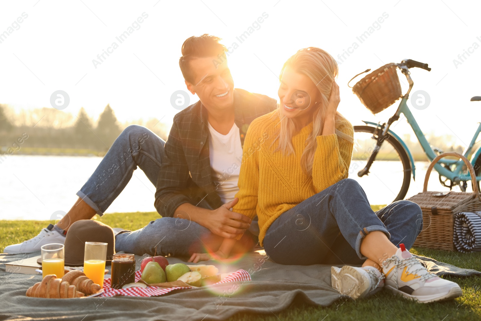 Photo of Happy young couple having picnic near lake on sunny day