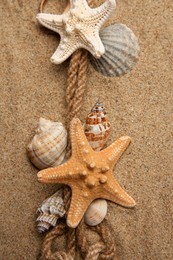 Photo of Beautiful sea stars, shells and rope on sand, flat lay