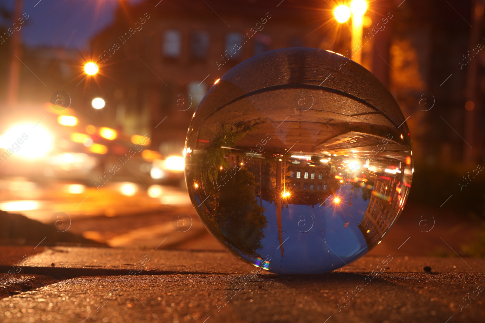 Photo of Beautiful city street, overturned reflection. Crystal ball on asphalt road at night, closeup