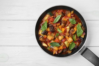 Frying pan with tasty ratatouille on white wooden table, top view. Space for text