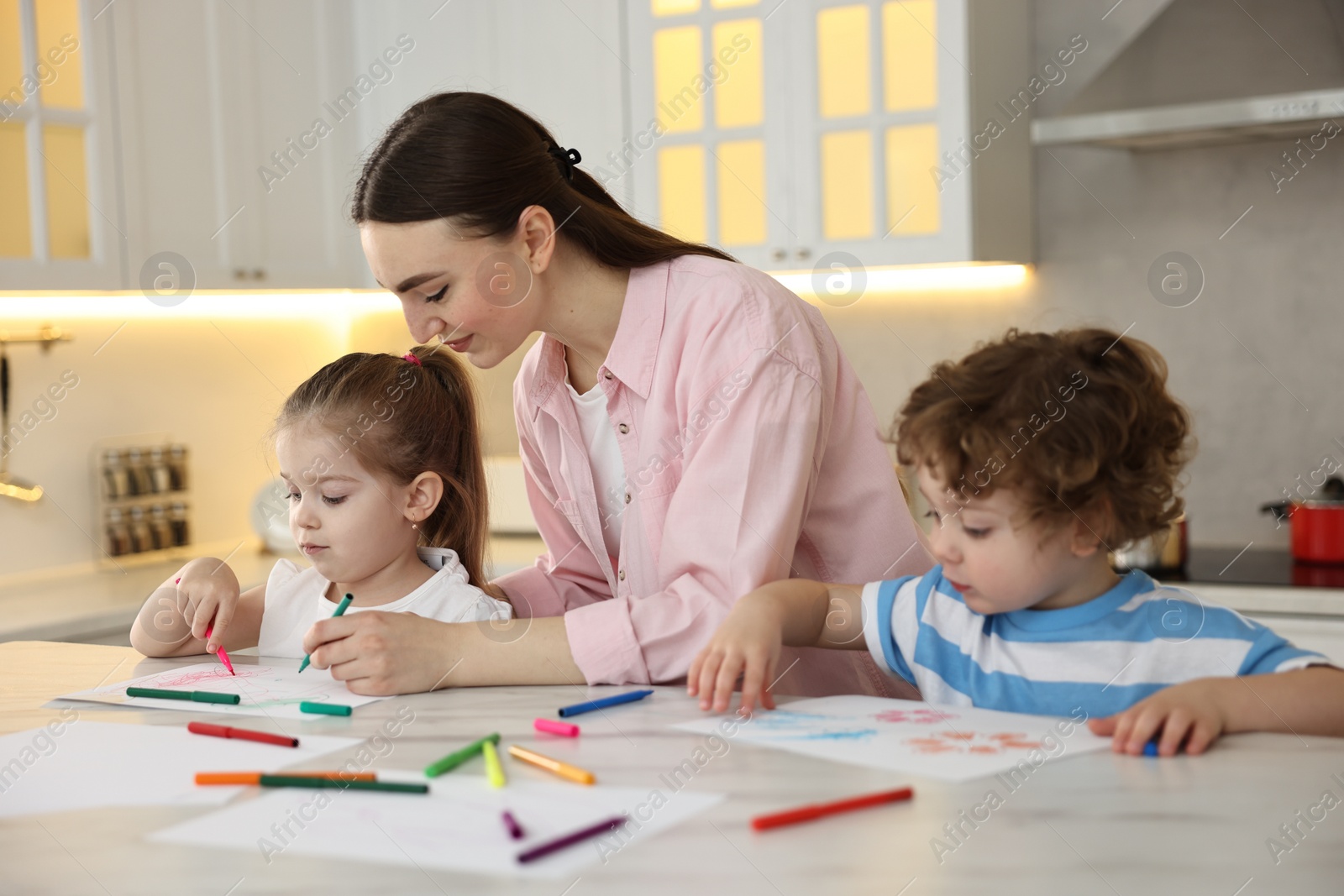 Photo of Mother and her little children drawing with colorful markers at table in kitchen