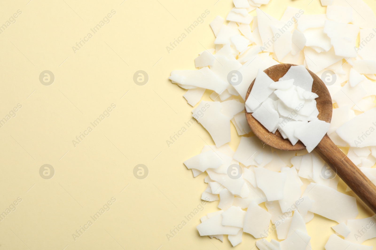 Photo of Wooden spoon and soy wax flakes on beige background, flat lay with space for text. Homemade candle material