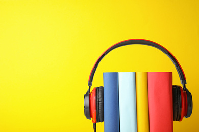 Photo of Books with modern headphones on yellow background. Space for text