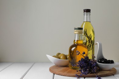 Different cooking oils and ingredients on white wooden table against light background, space for text