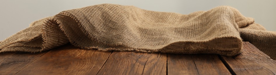 Natural burlap fabric on wooden table against light background. Space for text