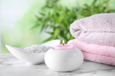 Composition with sea salt, candle and towels on white marble table against blurred background. Spa concept