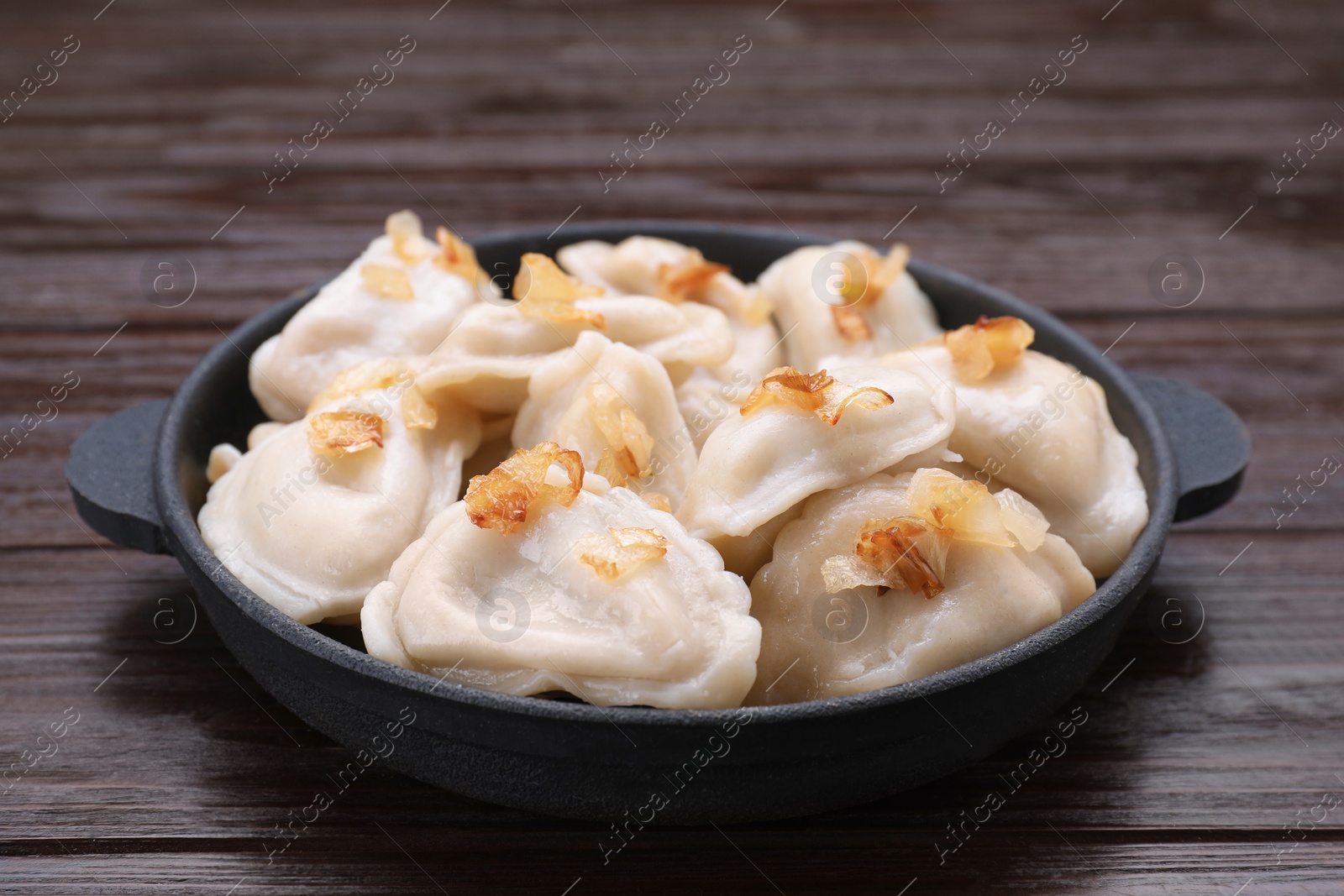 Photo of Delicious dumplings (varenyky) with potatoes and onion on brown wooden table