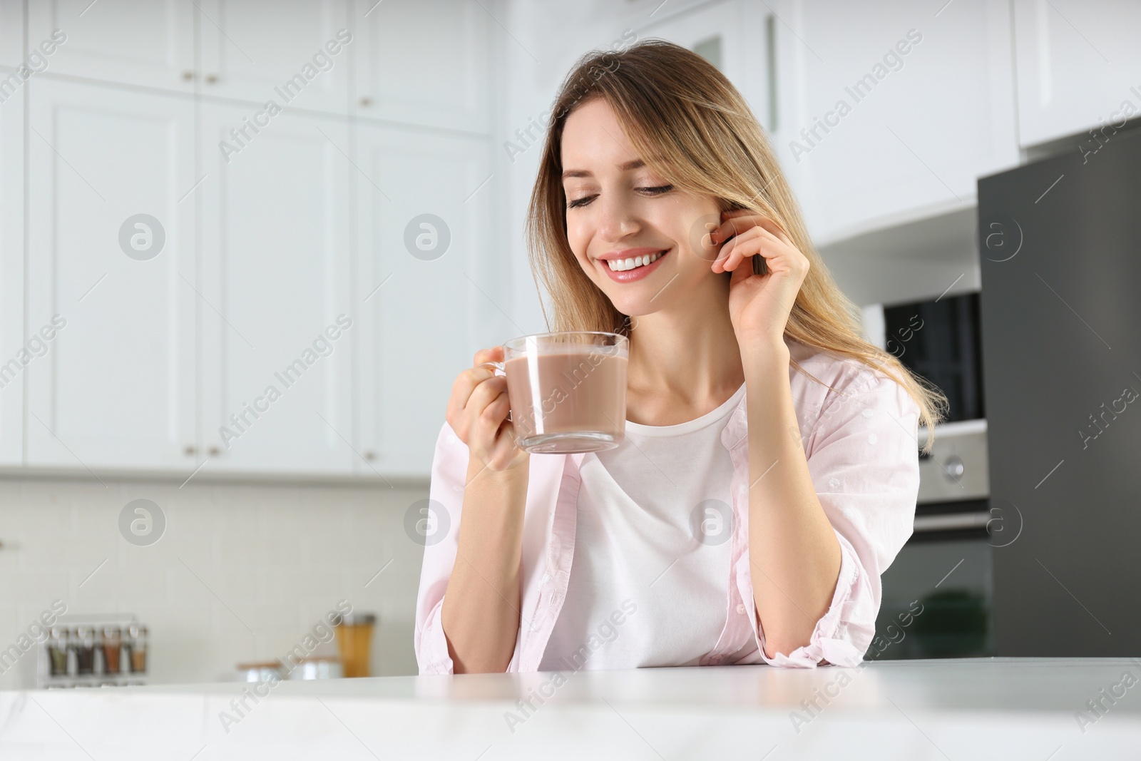 Photo of Young woman with glass cup of chocolate milk in kitchen