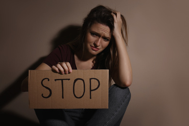 Photo of Crying young woman with sign STOP near beige wall. Domestic violence concept