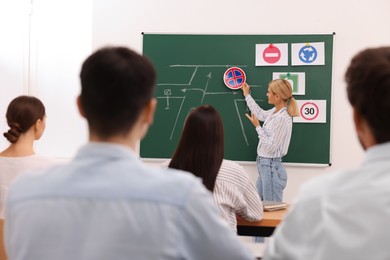 Teacher showing No Stopping road sign near chalkboard during lesson in driving school