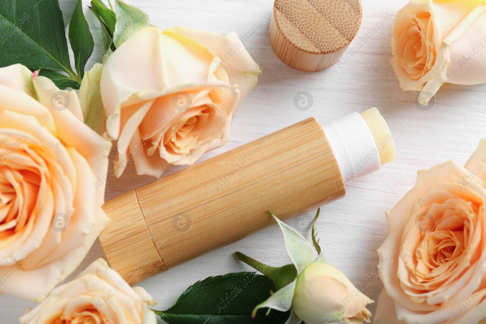 Photo of Lip balm and rose flowers on white wooden background, flat lay