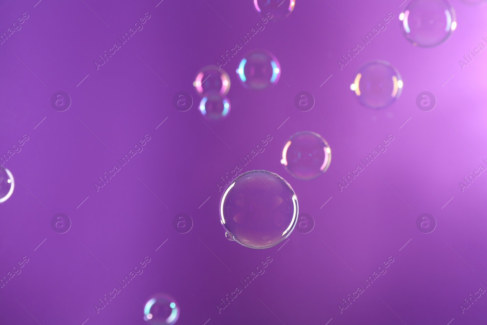 Photo of Beautiful transparent soap bubbles on violet background