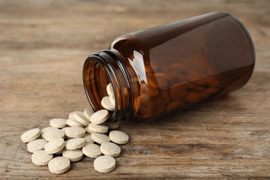 Bottle with vitamin pills on wooden table, closeup
