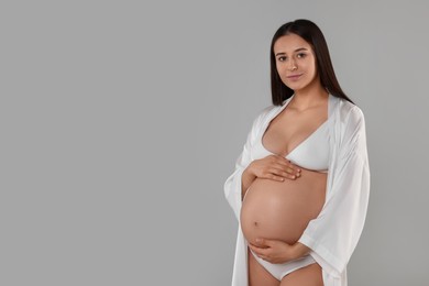 Photo of Beautiful pregnant woman in stylish comfortable underwear and robe on grey background, space for text