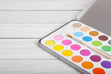 Photo of Watercolor palette with brush on white wooden table, closeup. Space for text