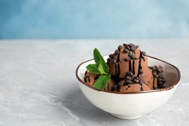Photo of Bowl of chocolate ice cream and mint on grey table, space for text