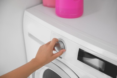 Photo of Woman turning on washing machine in bathroom, closeup. Laundry day