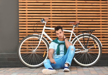 Handsome young hipster man with bicycle near wooden wall outdoors