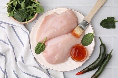 Photo of Marinade, basting brush and raw chicken fillets on white table, flat lay