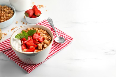 Bowl with tasty granola and strawberries served on white table. Space for text