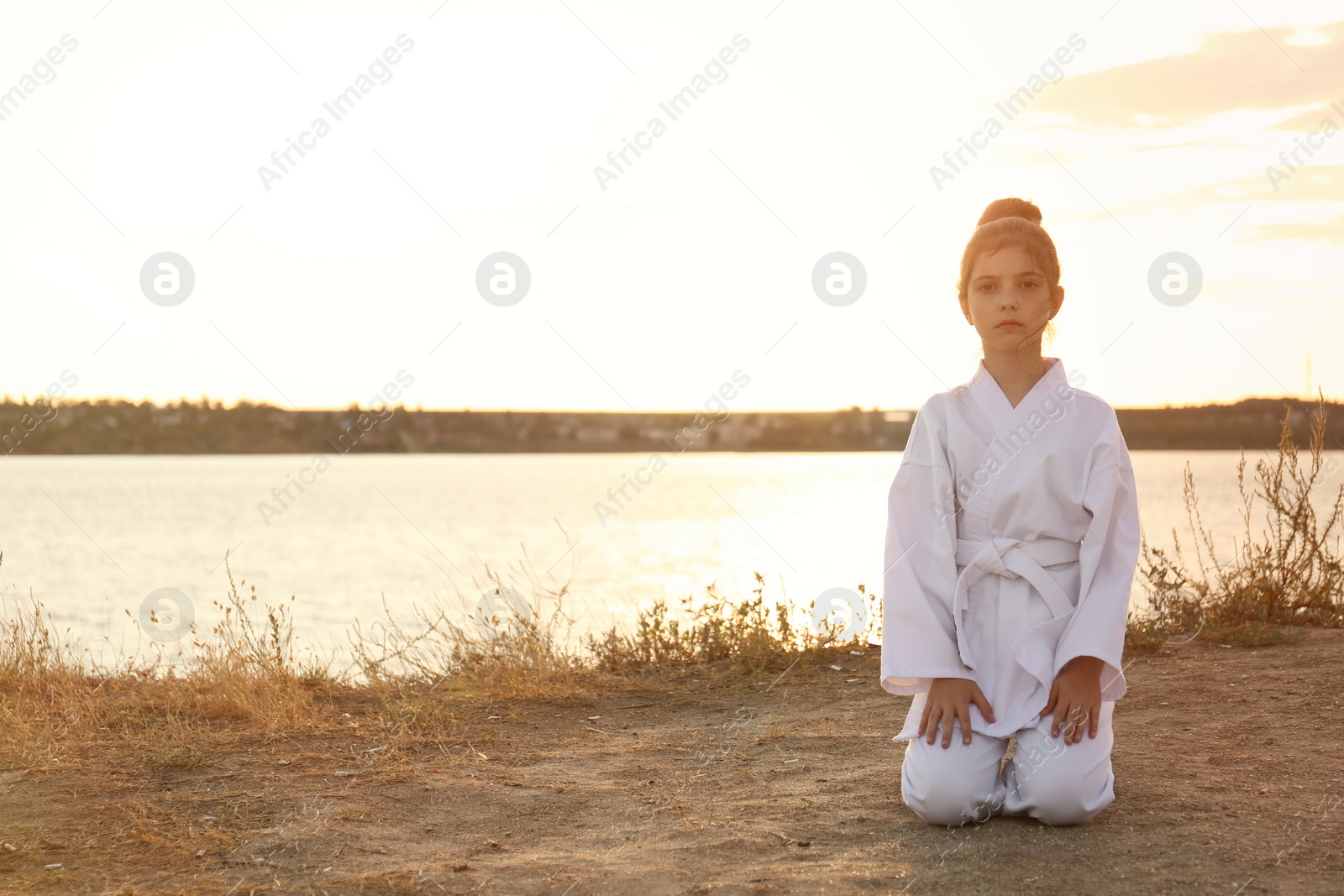 Photo of Cute little girl in kimono meditating near river at sunset. Karate practicing