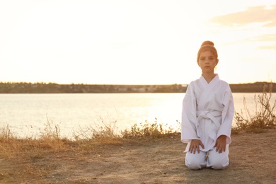 Photo of Cute little girl in kimono meditating near river at sunset. Karate practicing