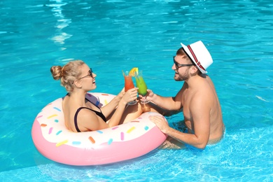 Young couple with refreshing cocktails and inflatable ring in swimming pool