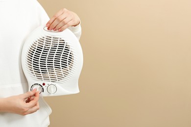 Photo of Young woman adjusting temperature on modern electric fan heater against beige background, closeup. Space for text