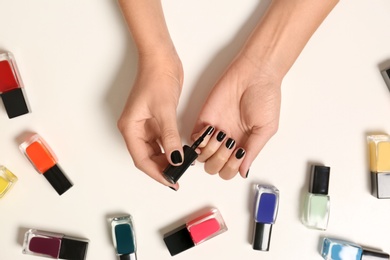 Woman applying nail polish near bottles on white background, top view