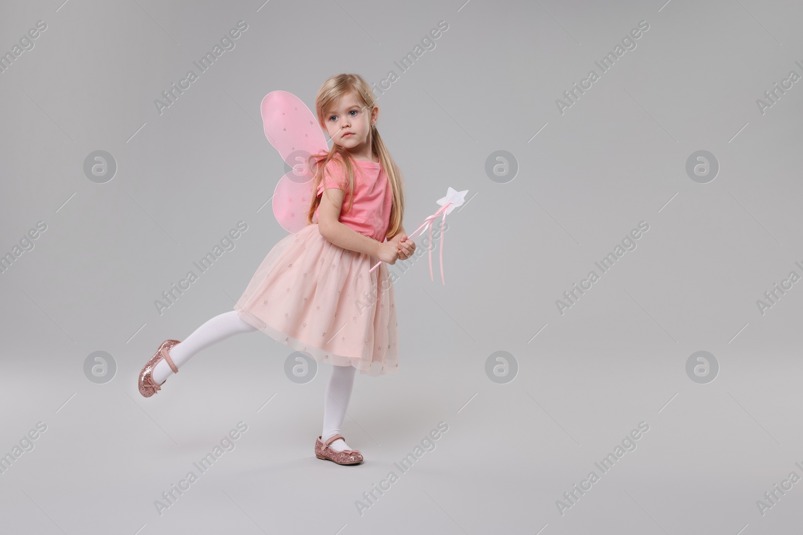 Photo of Cute little girl in fairy costume with pink wings and magic wand on light grey background, space for text