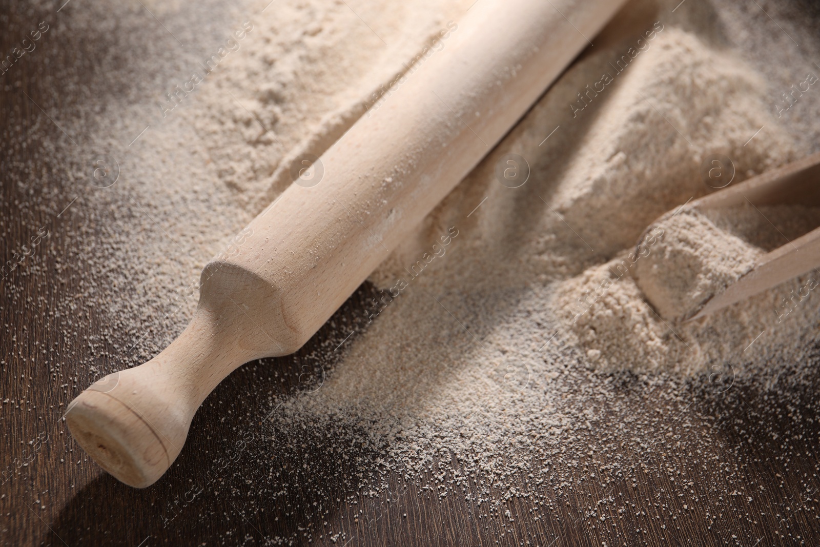 Photo of Pile of flour, rolling pin and scoop on wooden table, closeup