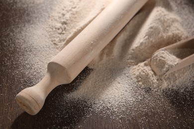 Pile of flour, rolling pin and scoop on wooden table, closeup