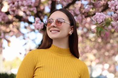 Beautiful woman in sunglasses near blossoming tree on spring day