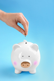 Photo of Woman putting coin into piggy bank on light blue background, closeup