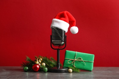 Photo of Microphone with Santa hat and decorations on grey table against red background. Christmas music