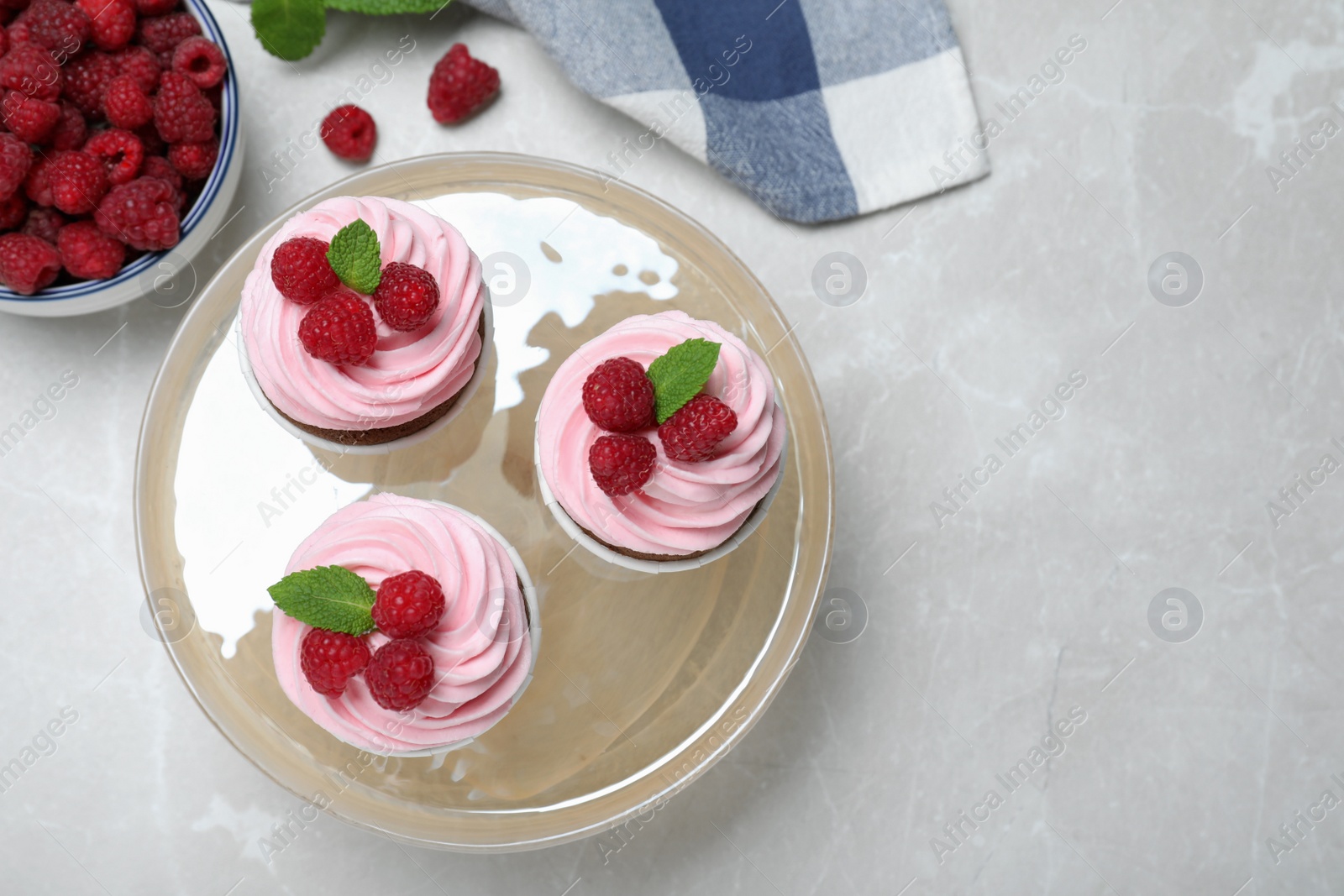 Photo of Delicious cupcakes with cream and raspberries on light grey marble table, flat lay. Space for text