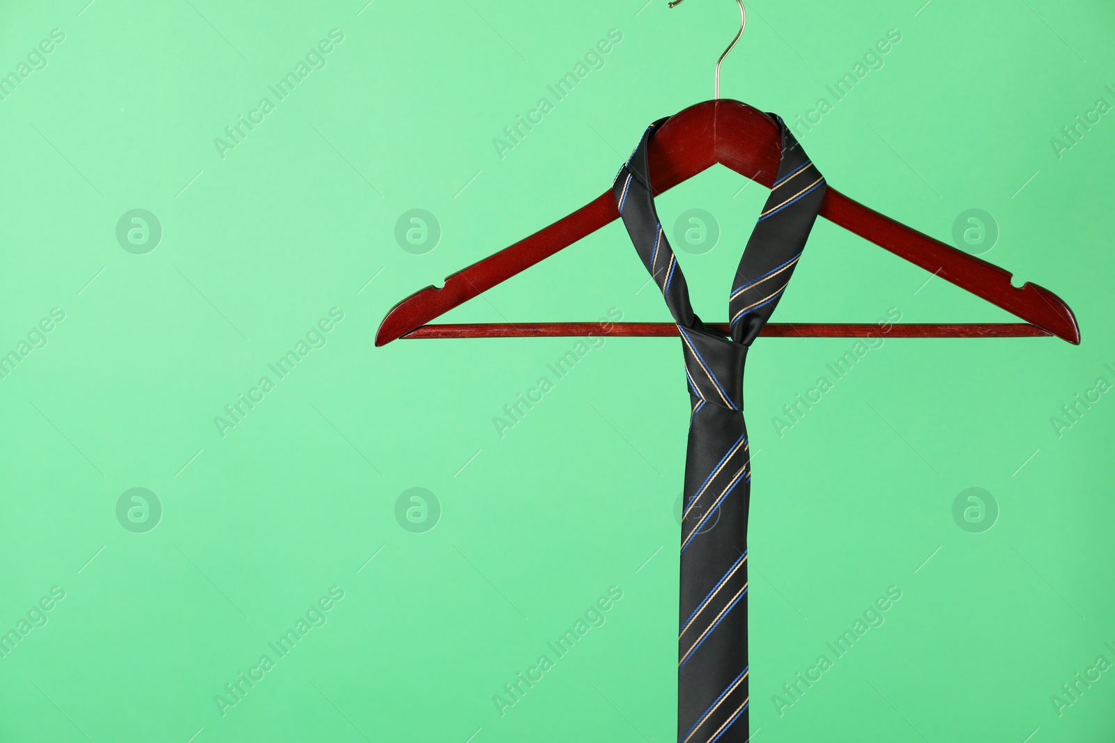 Photo of Hanger with black striped tie on green background. Space for text