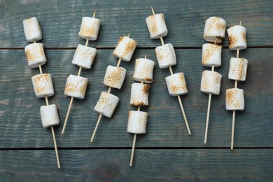 Photo of Sticks with roasted marshmallows on blue wooden table, flat lay