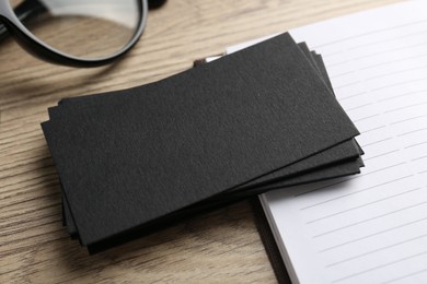 Photo of Blank black business cards and notebook on wooden table, closeup. Mockup for design