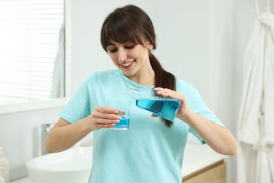 Photo of Young woman using mouthwash in bathroom. Oral hygiene