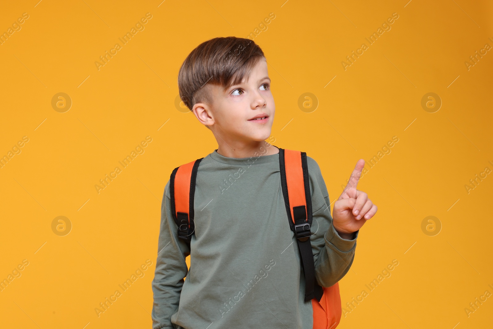 Photo of Cute schoolboy pointing upwards on orange background