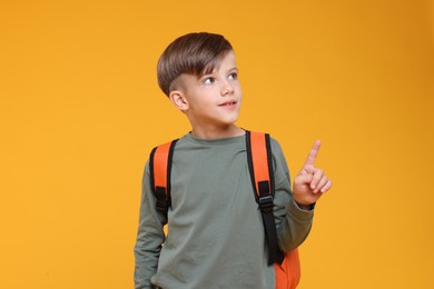 Photo of Cute schoolboy pointing upwards on orange background