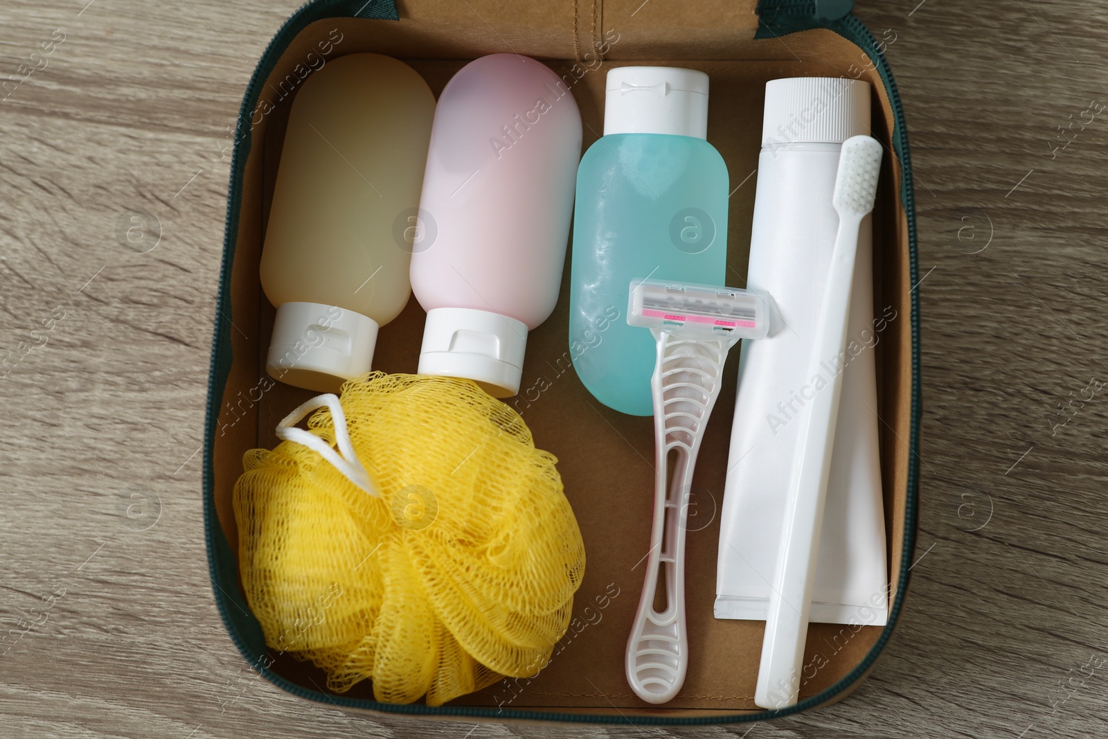 Photo of Cosmetic travel kit in compact toiletry bag on wooden table, top view. Bath accessories