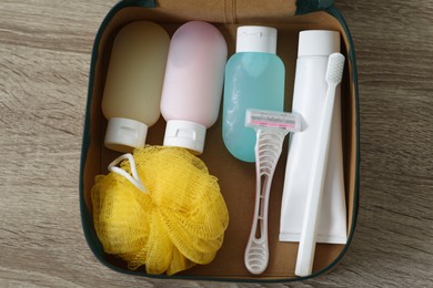 Photo of Cosmetic travel kit in compact toiletry bag on wooden table, top view. Bath accessories
