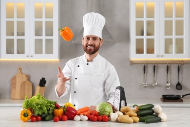 Photo of Portrait of professional chef throwing bell pepper near vegetables at marble table in kitchen
