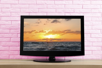 Image of TV screen with sunset sky over sea on table near pink wall