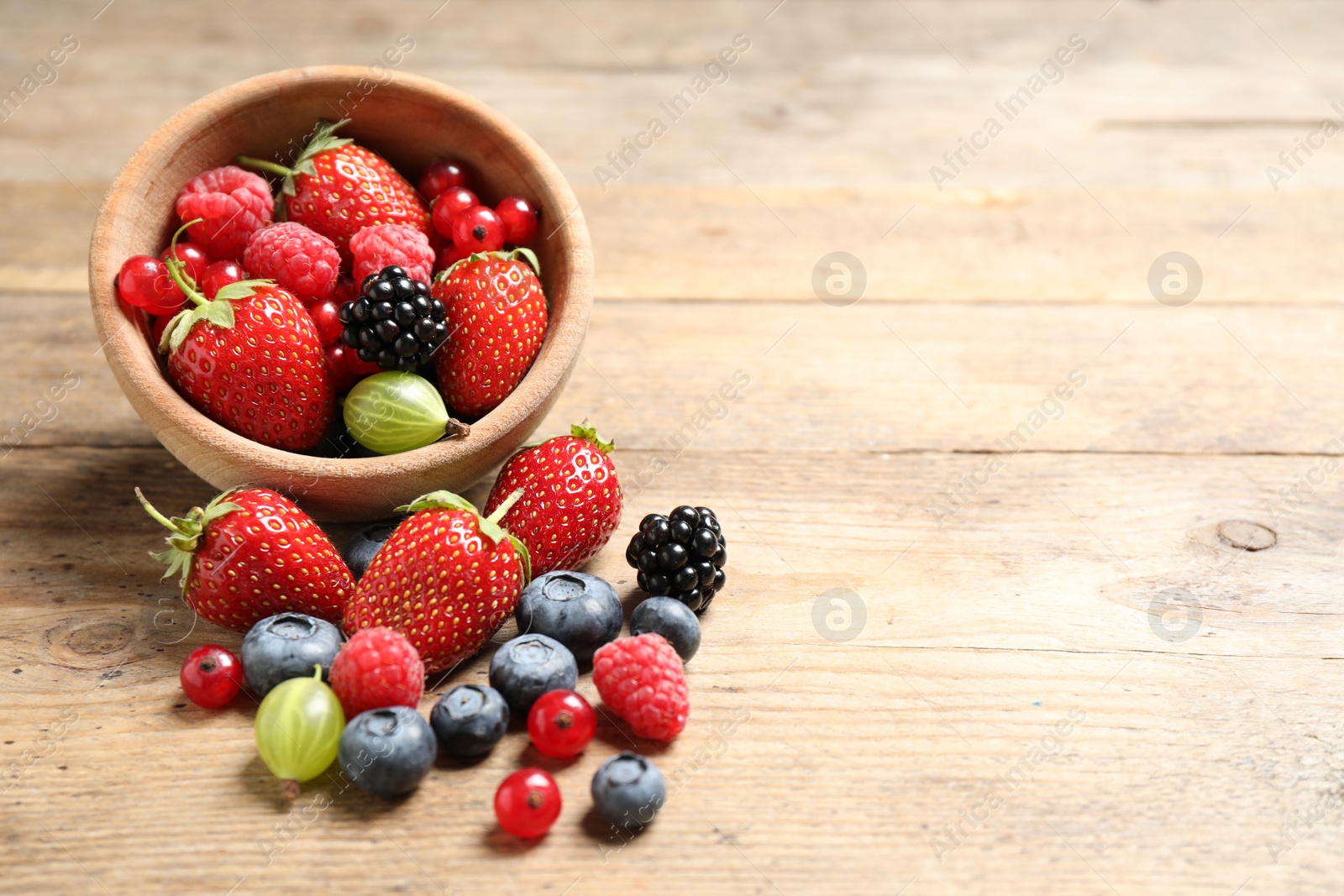 Photo of Mix of ripe berries on wooden table. Space for text