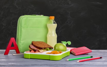 Image of Composition with lunch box and food on grey wooden table near blackboard